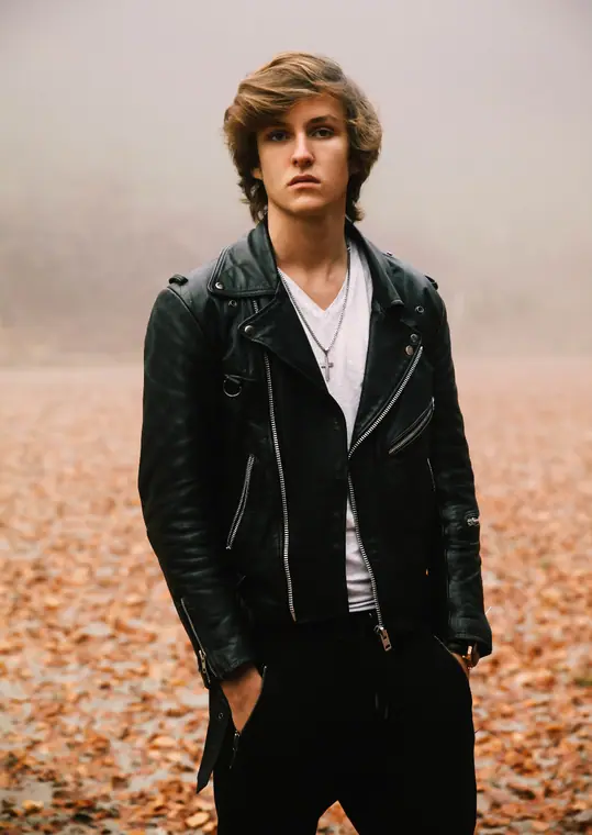 Young man in a leather jacket among autumn leaves